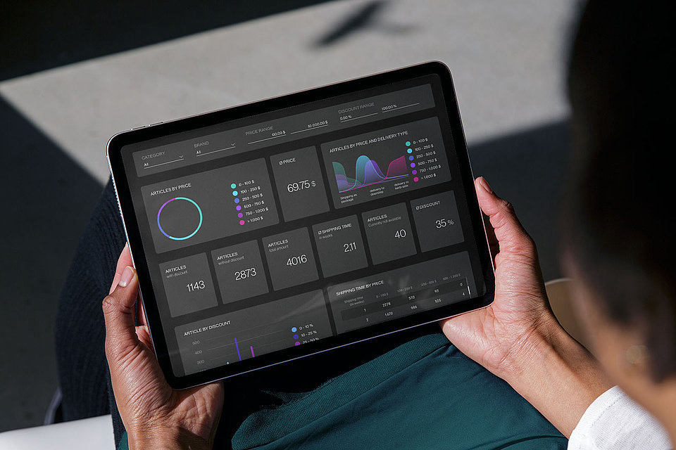 A woman holds a tablet with a dashboard of XPLN's BENCHMARKER software solution